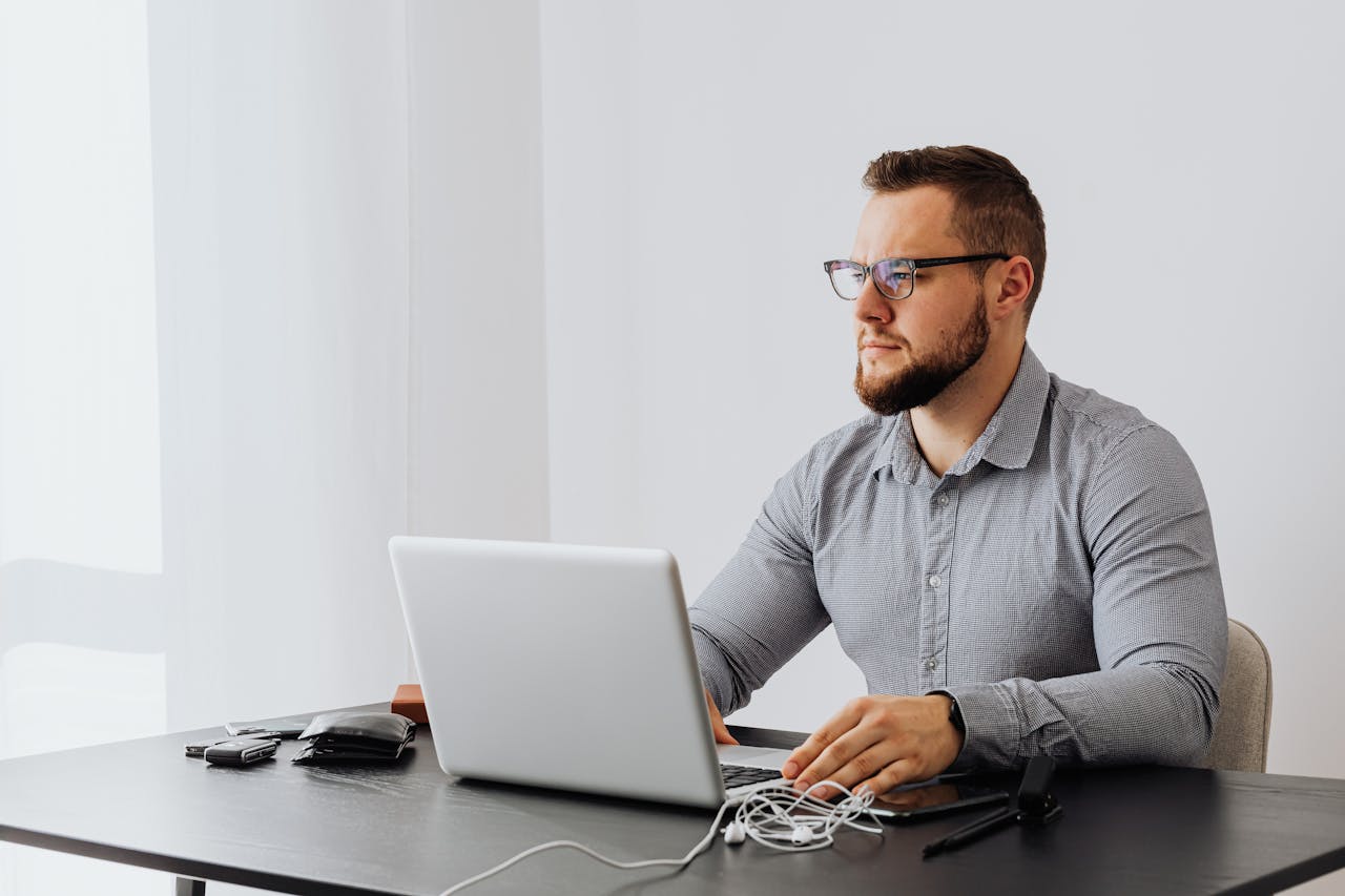 Services-02 Bearded man with eyeglasses working on a laptop in a minimalist office setting.